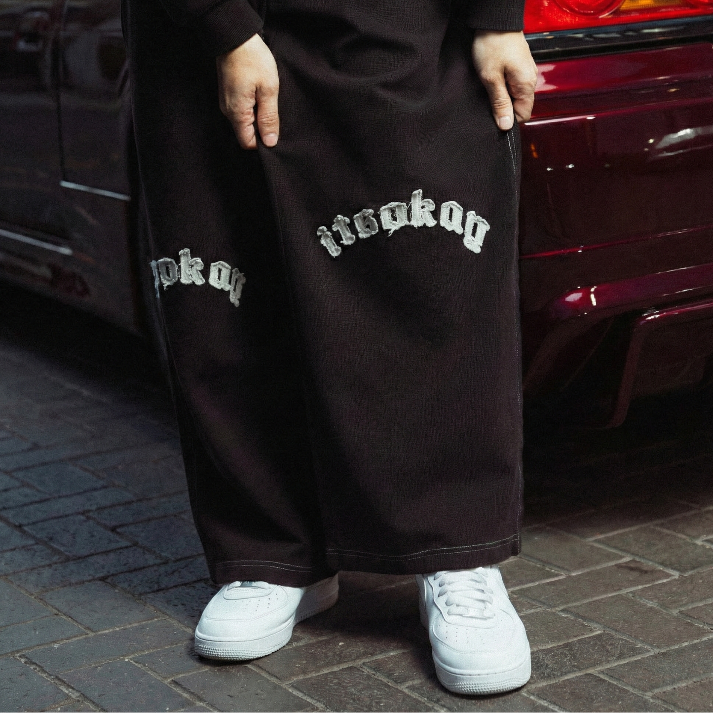 Person wearing black pants with white text standing next to a red car.