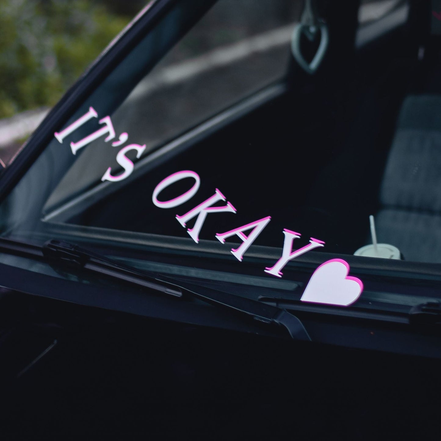 Car window with 'It's Okay' decal and heart shape sticker.