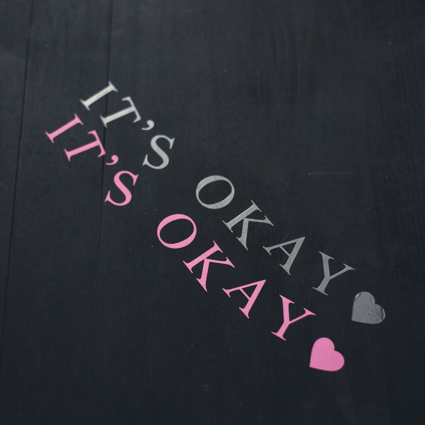 Text 'IT'S OKAY' with heart symbols on a black background
