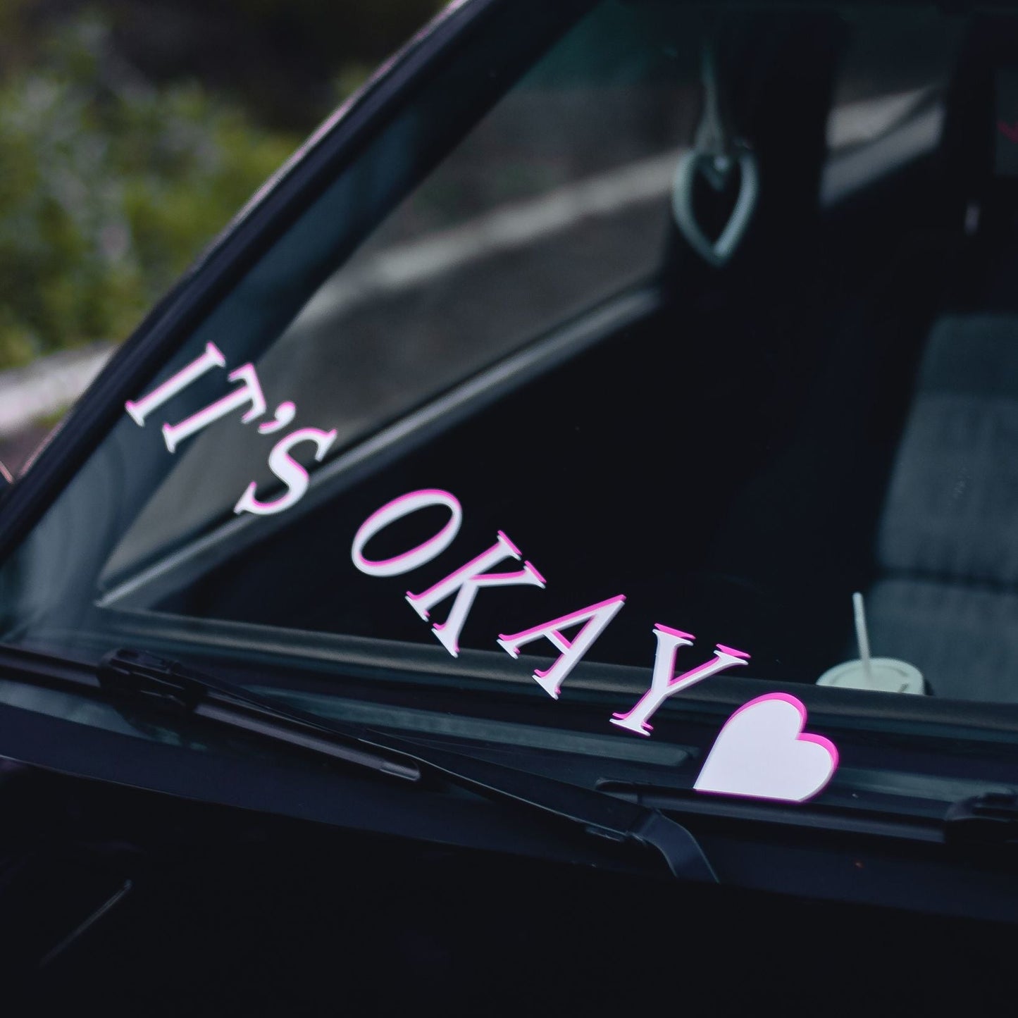 Car window with 'It's Okay' decal and heart symbol ok