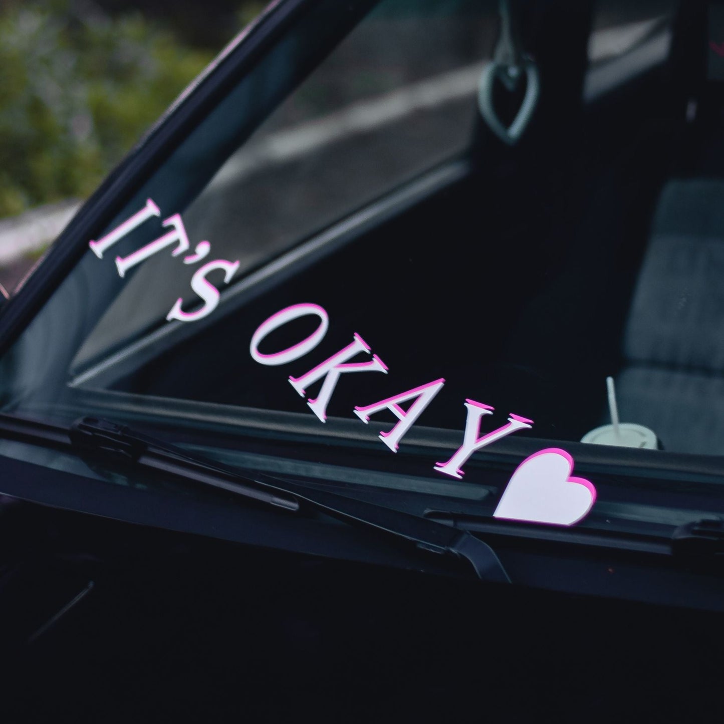 Car window with 'It's Okay' text and a heart sticker o