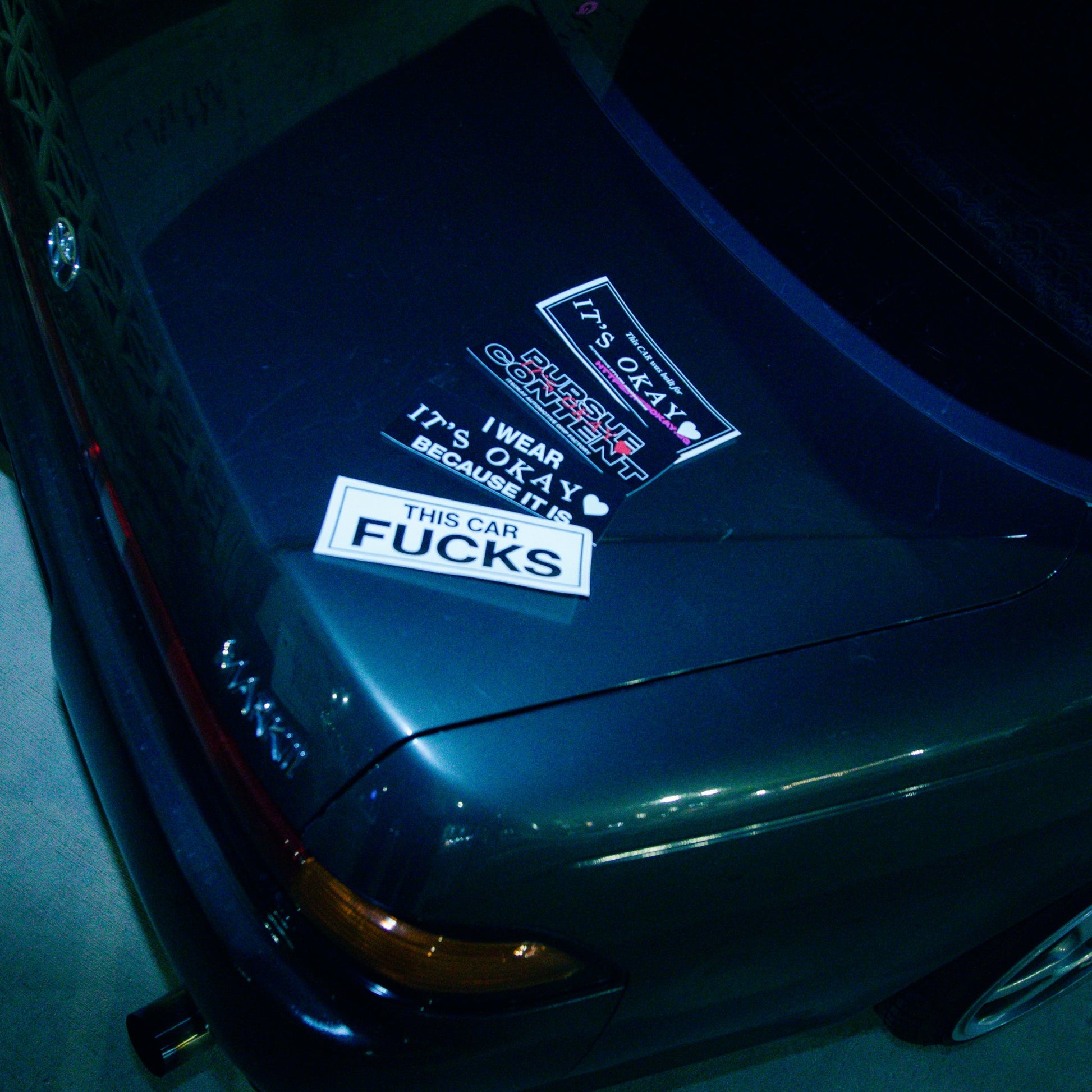 Close-up of a car's front bumper with visible stickers at night. Itsokay