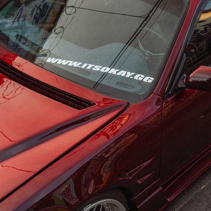 Close-up of a red car with a visible website address on the windshield.