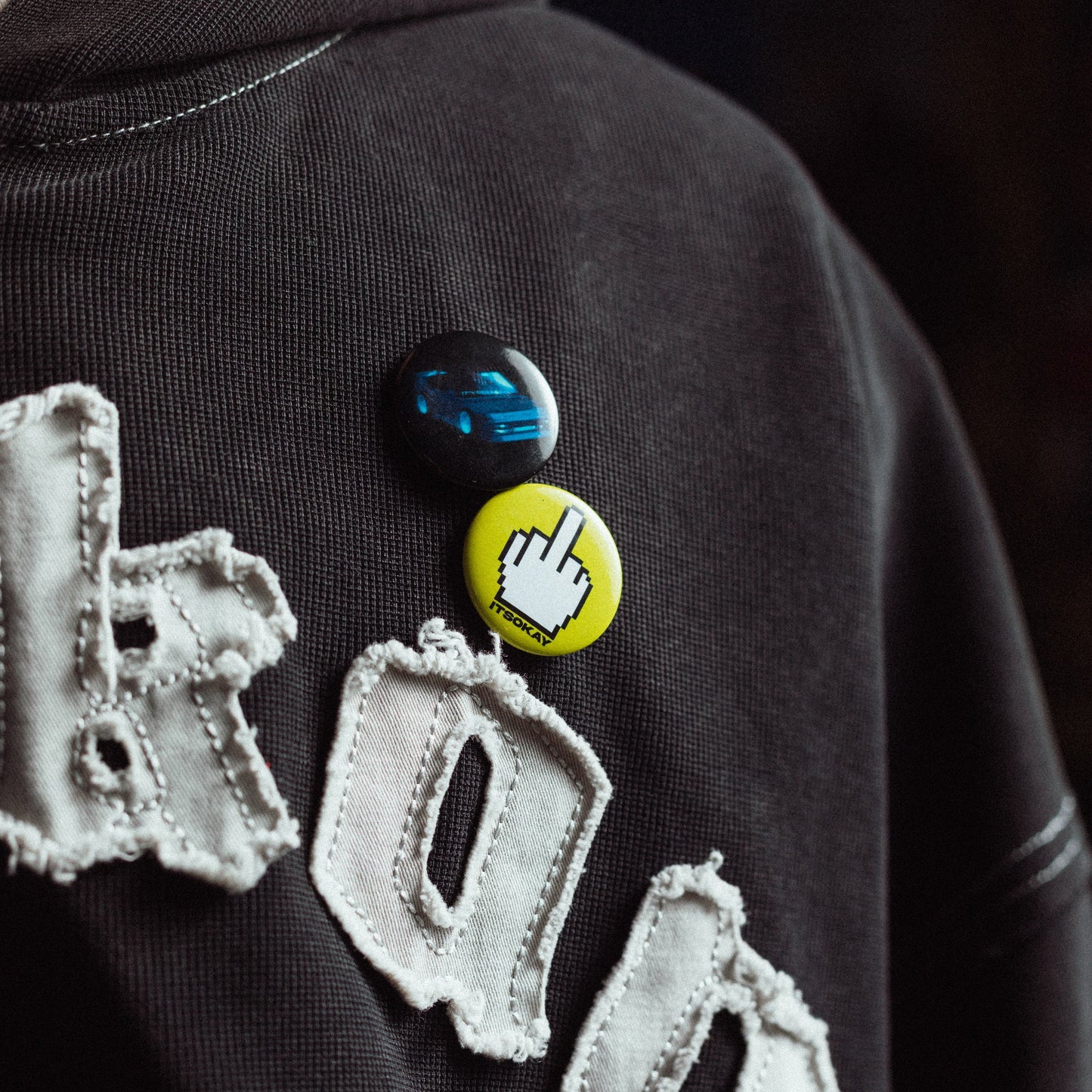 Black hoodie with decorative text and pins on a dark background