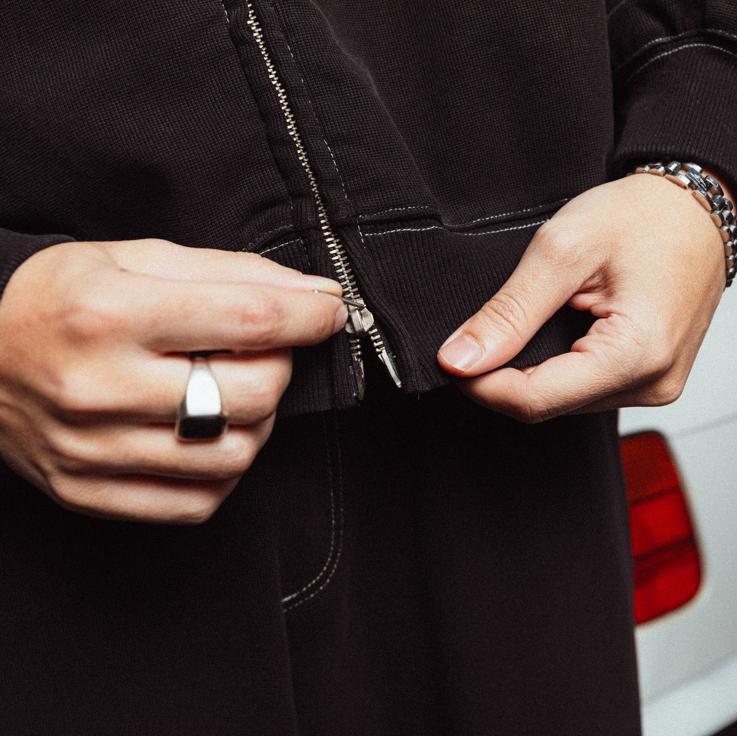 Person zipping a black jacket with a white vehicle in the background