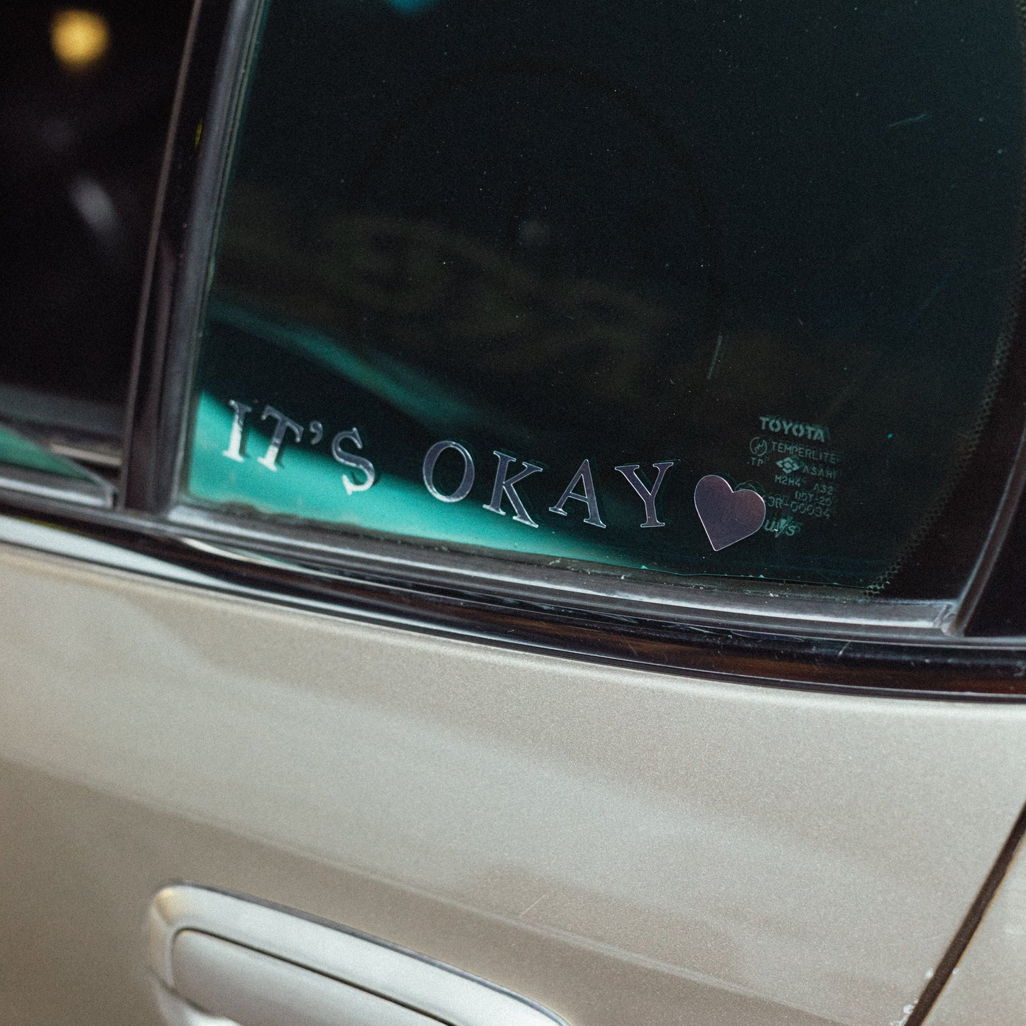 Car window with 'It's Okay' decal and heart symbol