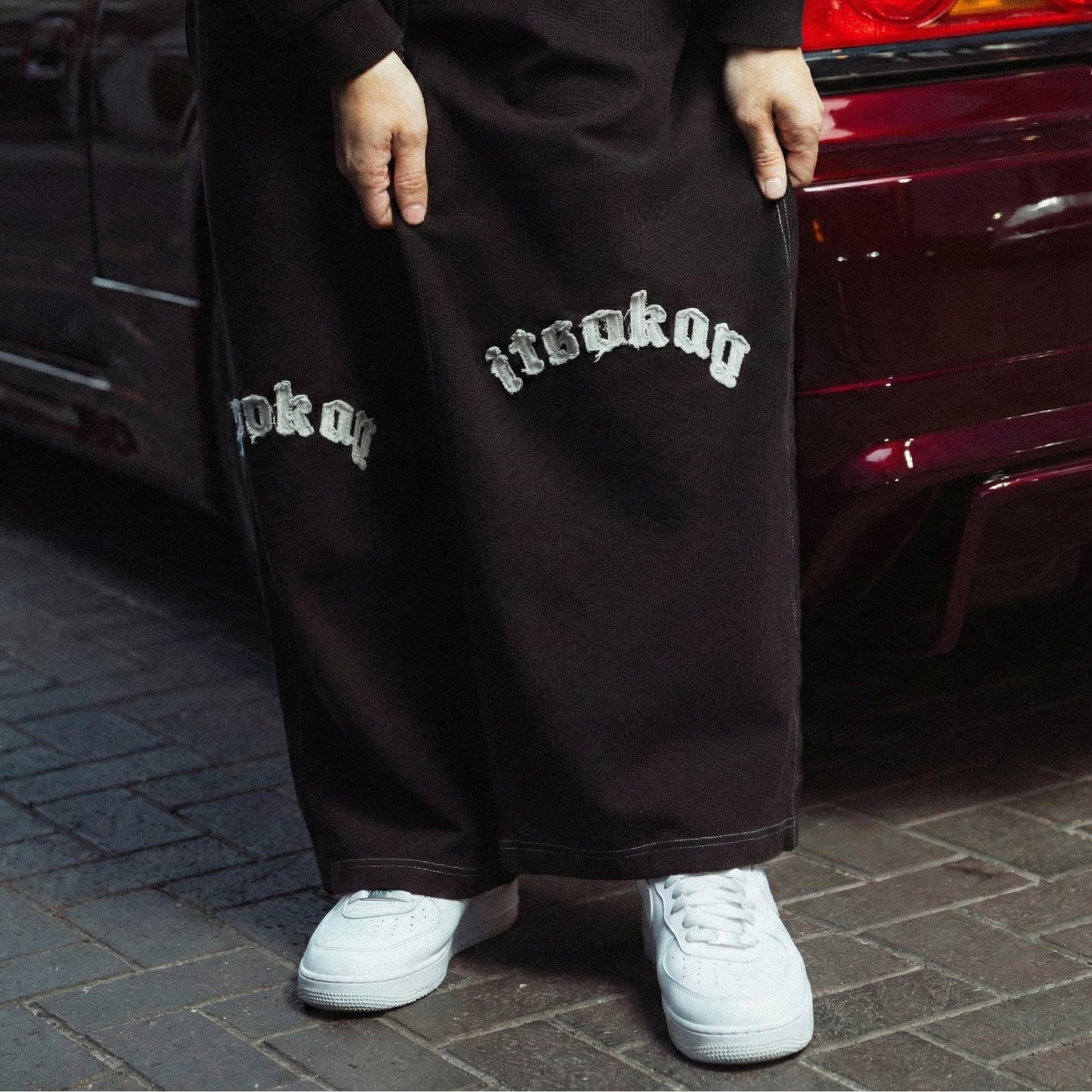 Person wearing black pants with white text standing next to a red car.